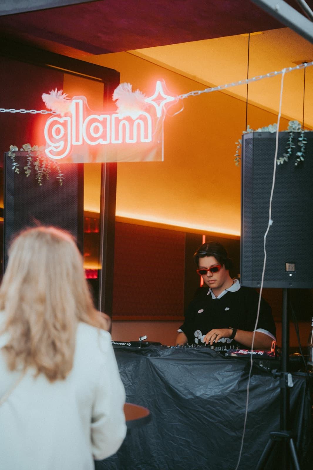 DJ behind the decks under the glam neon sign